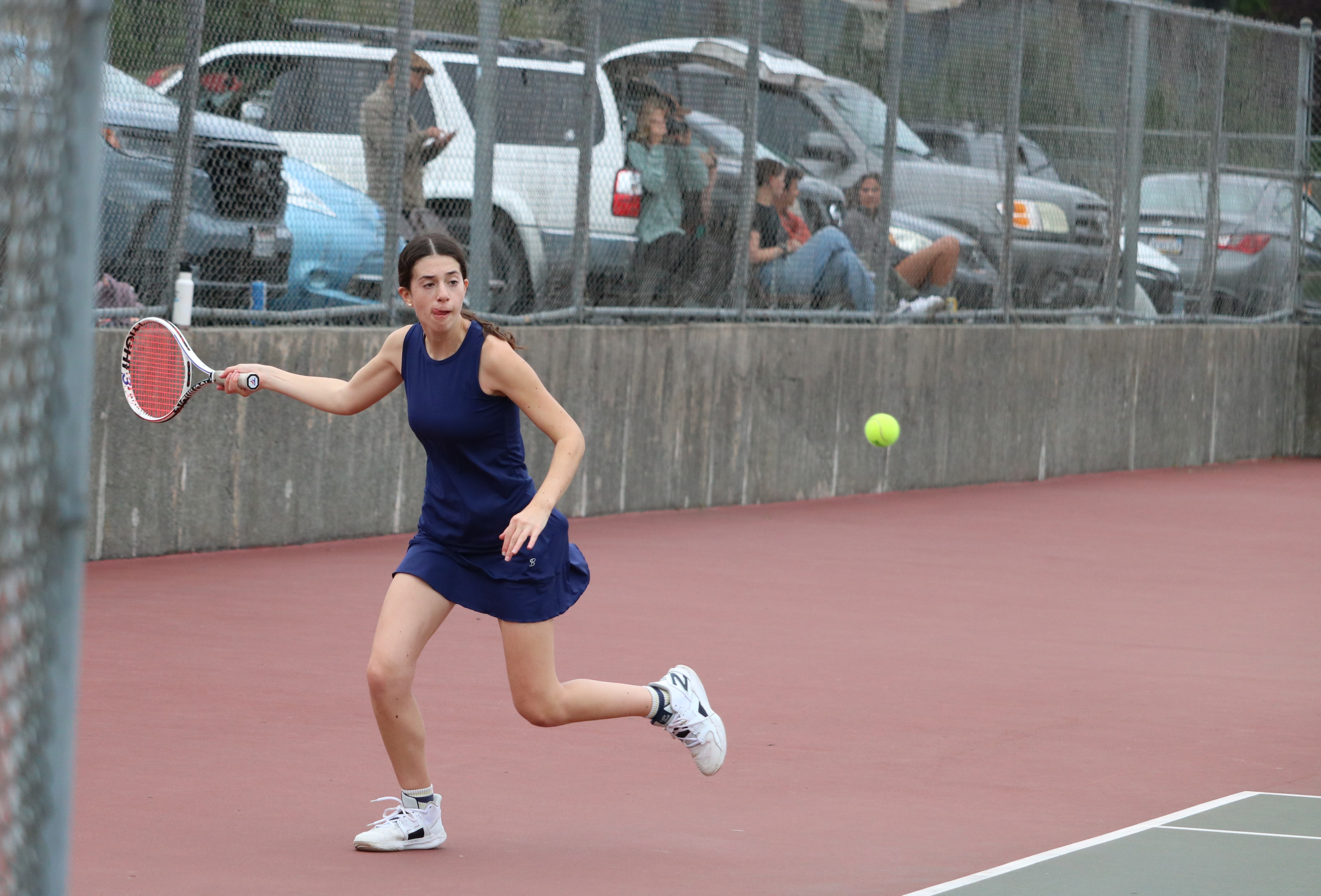 High school athlete plays tennis in a navy uniform. 